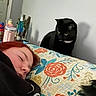 Wiz is registered to the contest to win money with this photo: person, sleeping, cat, black_cat, pillow, floral_pattern, bedroom, indoor, resting, curious, red_hair, blanket, face, animal, pet, quiet, relaxation, furniture, home, peaceful