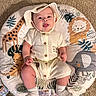 Evan is registered to the contest to win money with this photo: baby, baby_accessory, buttons, carpet, chubby_legs, cozy, cute, elephant_illustration, giraffe_illustration, hat, indoor, infant, leaves_pattern, lion_illustration, onesie, playmat, portrait, smiling, socks, tongue_out