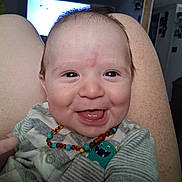 Ledger joined the competition — help win amazing prizes! baby, infant, smiling, laughing, amber_necklace, onesie, striped_clothing, monster_patch, close_up, face, eyes, tongue, cheeks, knees, legs, indoor, living_room, ceiling_fan, television, happy