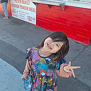 Dulcinea joined the competition — help win amazing prizes! child, smiling, peace_sign, colorful_dress, halloween_theme, sidewalk, red_wall, menu, outdoor, casual_clothing, person, happy, young_girl, holding_bottle, concrete, urban, daylight, long_hair, playful, cute