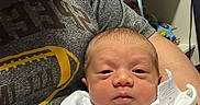 Luis is registered to the contest to win money with this photo: newborn, baby, infant, person, adult, clothing, blanket, tshirt, football, room, shelf, toy, fan, water_bottle, panda_toy, stuffed_animal, home, indoor, holding, portrait