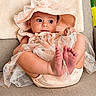 adorable, baby, barefoot, child, couch, curious, cute, fabric, furniture, hat, home, indoors, infant, peach_outfit, plush, portrait, relaxed, seated, small_feet, soft