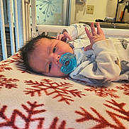 Easton is registered to the contest to win money with this photo: baby, pacifier, blanket, snowflake_pattern, infant, bed, nursery, hospital, clothing, face, hand, skin, comfort, resting, indoors, young_child, expression, cute, newborn, lying_down