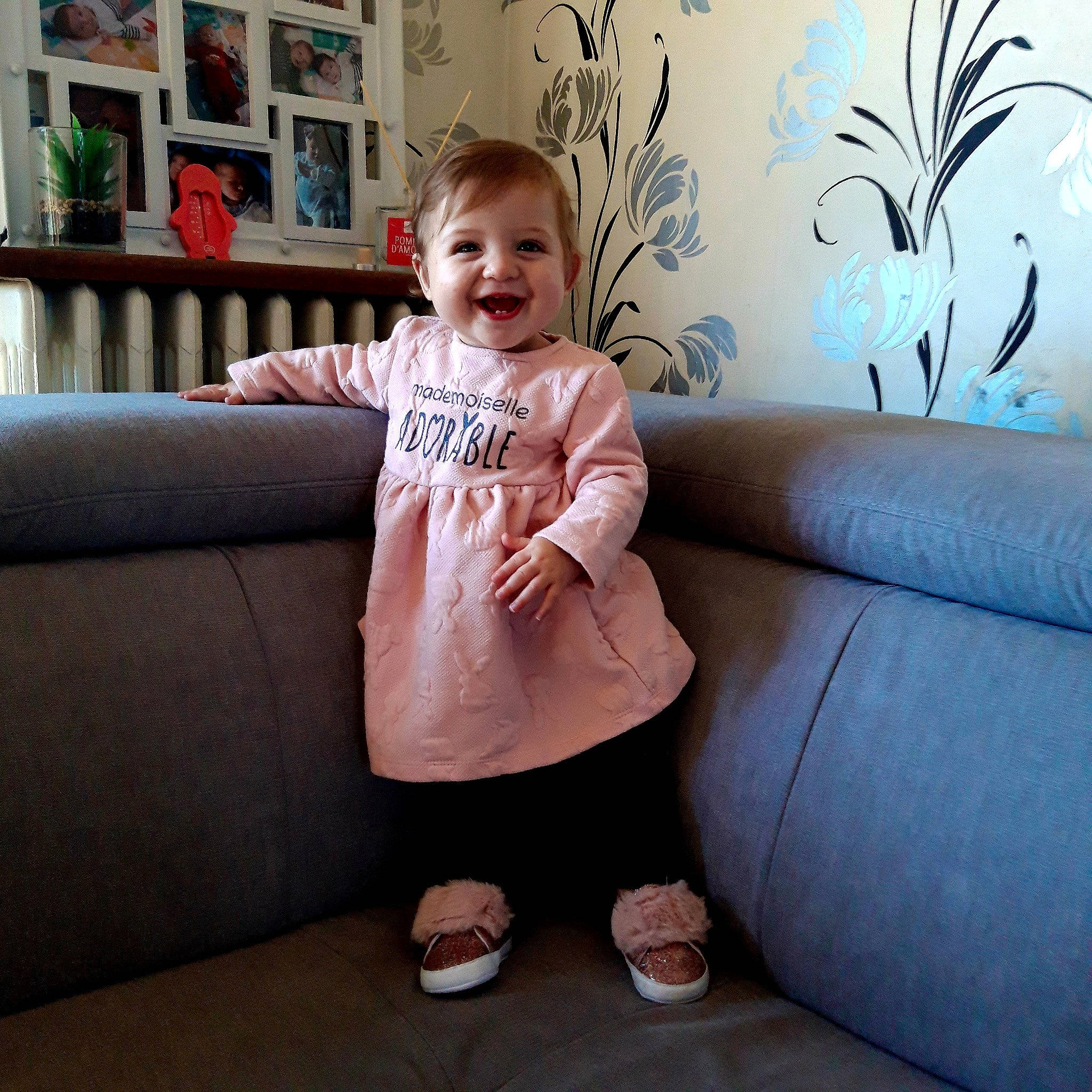 Victoria a rejoint le concours — aidez-le/la à gagner de superbes lots ! baby_toddler_clothing, bookcase, comfort, couch, floor, flooring, happy, human_leg, joy, knee, leg, living_room, person, picture_frame, rectangle, room, shelf, sleeve, smile, studio_couch