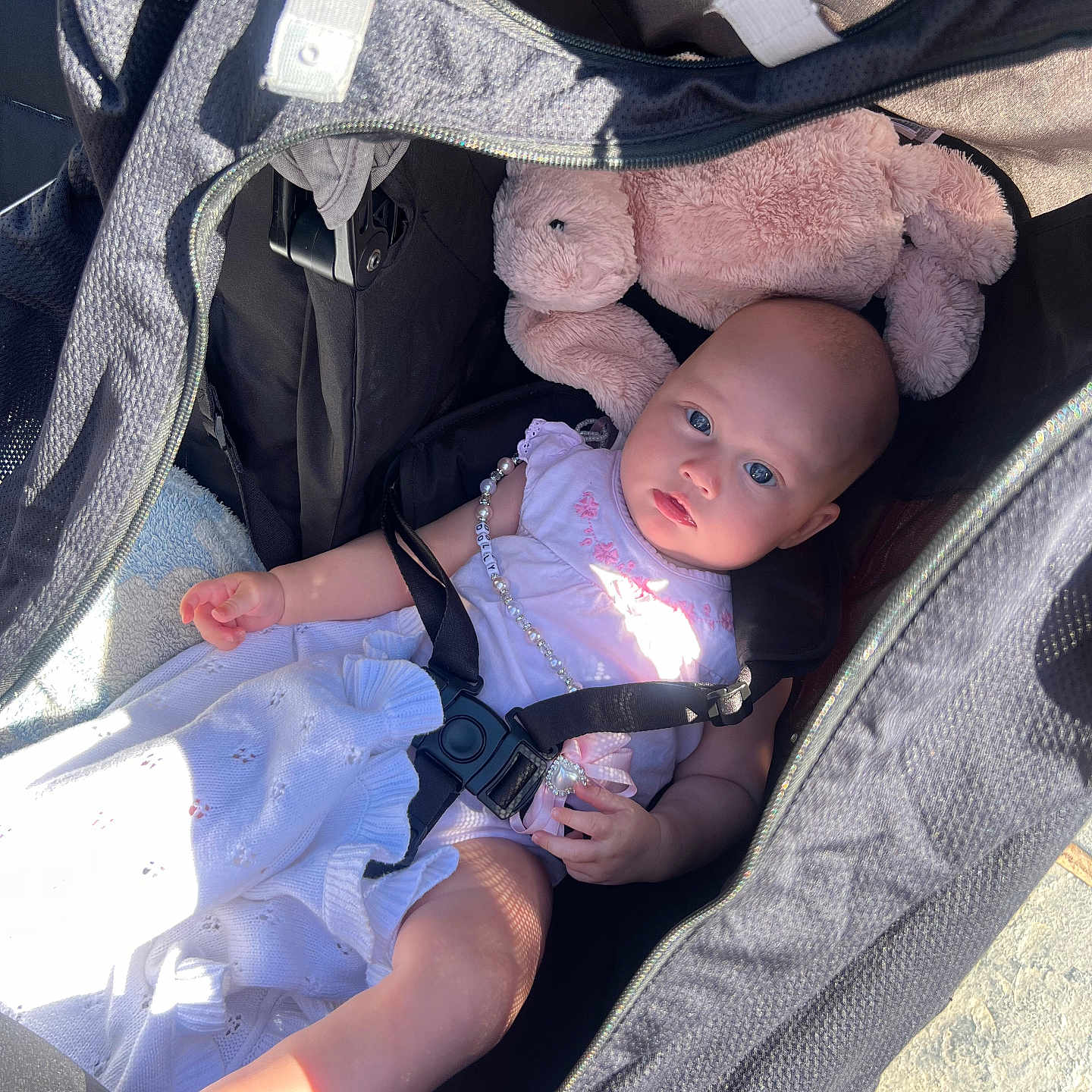 Dolly joined the competition — help win amazing prizes! baby, child, comfort, curious, face, floor, footwear, hand, infant, necklace, outdoor, pink_bunny, plush_toy, portrait, relaxation, seatbelt, shadow, stroller, sunlight, white_clothing