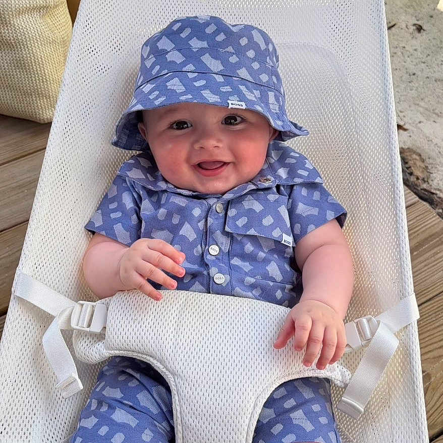 Nahil a rejoint le concours — aidez-le/la à gagner de superbes lots ! baby, child, smiling, blue_outfit, bucket_hat, baby_chair, mesh_chair, outdoor, plants, wooden_deck, happy, infant, summer_clothing, baby_fashion, cute, sitting, daylight, portrait, person, sunlight