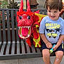 bench, boy, casual, chairs, child, concrete, daytime, dragon_puppet, outdoor, people, plants, playful, public_space, sandals, shorts, smiling, table, toy, tshirt, urban