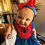 baby, blue_dress, child, cute, eyes, face, furniture, hand, happy, headband, holding, home, indoor, person, portrait, red_bow, smiling, spiderman_dress, toddler, wall_art