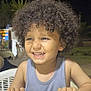 background_blur, child, curly_hair, cute, expression, face, hands, happy, night, outdoor, person, portrait, seated, skin, smiling, table, tank_top, toddler, white_table, young