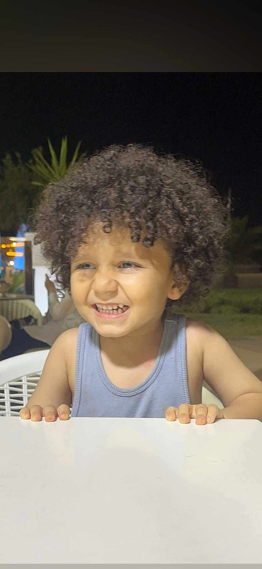 Chahyne participe au concours pour gagner de l'argent avec cette photo : background_blur, child, curly_hair, cute, expression, face, hands, happy, night, outdoor, person, portrait, seated, skin, smiling, table, tank_top, toddler, white_table, young