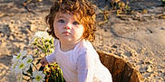 Marlee is registered to the contest to win money with this photo: toddler, child, curly_hair, blue_eyes, white_clothing, wooden_bucket, daisies, flowers, outdoor, sand, sunlight, portrait, baby, nature, cute, innocent, garden, daylight, person, flower_arrangement