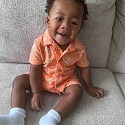 Symere joined the competition — help win amazing prizes! toddler, child, smiling, sitting, orange_outfit, white_socks, couch, indoor, happy, cute, curly_hair, infant, person, portrait, casual_clothing, baby, young_child, cozy, comfortable, home