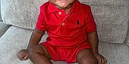 Symere joined the competition — help win amazing prizes! toddler, child, smiling, red_clothing, polo_shirt, shorts, checkered_shoes, sitting, couch, indoor, happy, cute, person, footwear, curly_hair, comfortable, portrait, infant, skin, young