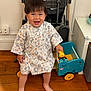 toddler, child, smiling, barefoot, toy, robe, wooden_floor, indoor, stroller, blue_toy_cart, happy, person, young_child, clothing, furniture, playtime, home, floor, cute, standing