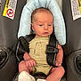 baby, infant, car_seat, onesie, socks, safety_harness, warning_labels, soft_pillow, cute, newborn, child, seat_belt, infant_clothing, indoors, person, baby_face, baby_hands, baby_legs, baby_feet, car_seat_pillow