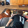 Homer is registered to the contest to win money with this photo: dog, boy, tablet, couch, indoor, wooden_cabinet, balloons, rug, dog_toy, floor, black_shirt, relaxed, pet, side_by_side, leisure, screen, casual, home, carpet, resting