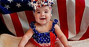 Camila joined the competition — help win amazing prizes! baby, child, smiling, patriotic, american_flag, headwear, bow, clothing, sitting, white_blanket, footwear, shoes, happy, blue_eyes, infant, cute, red_white_blue, stars, stripes, portrait