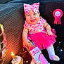 baby, infant, smiling, pink_tutu, bow_headband, birthday_cupcake, lit_candle, barbie_packaging, birthday_ribbon, toy, sitting, couch, celebration, party, white_tights, happy, cute, sprinkles, stars_confetti, portrait