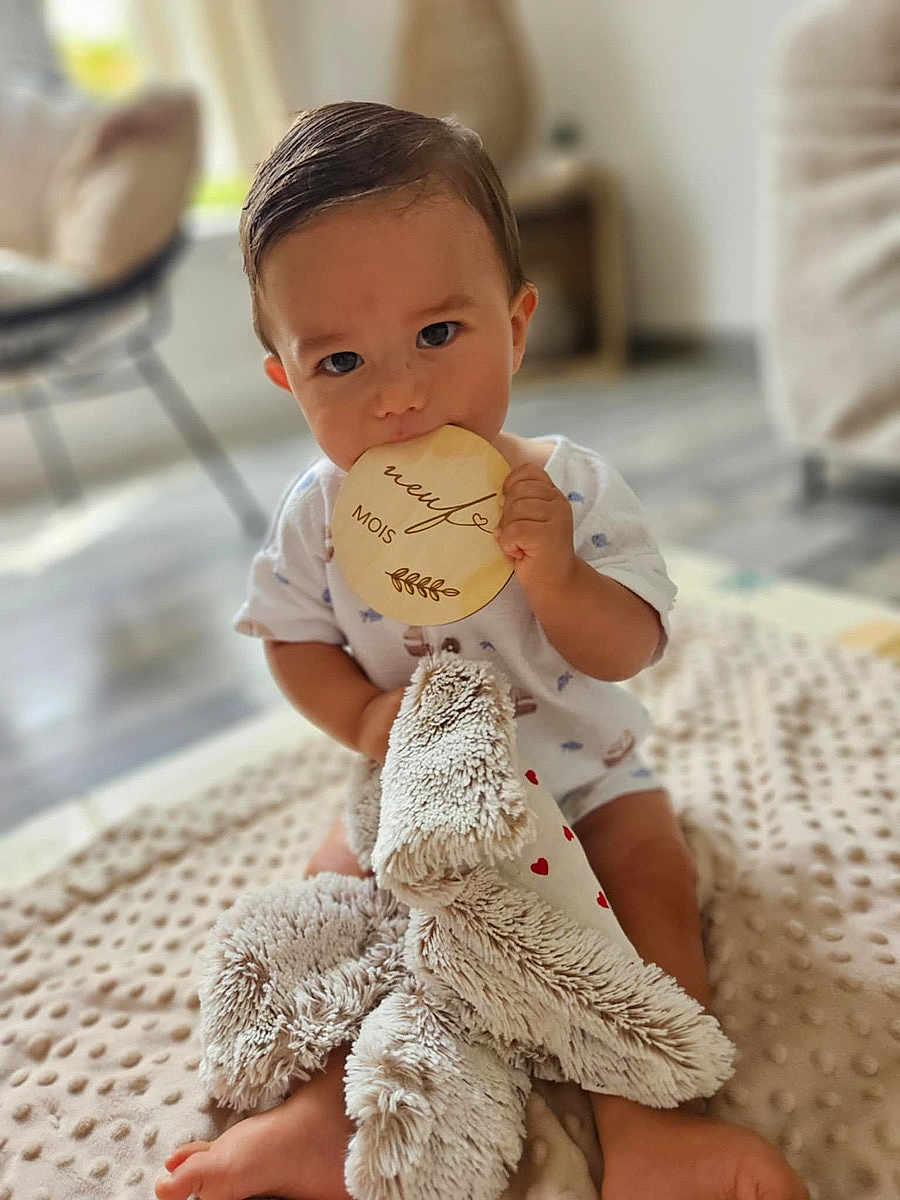 Taïan a rejoint le concours — aidez-le/la à gagner de superbes lots ! baby, blanket, blurred_background, child, comfort, cute, face, feet, floor, hands, home, indoor, infant, milestone_marker, nibbling, plush_toy, short_sleeve, sitting, soft_toy, wooden_milestone