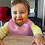 toddler, child, food, messy, spaghetti_sauce, bib, table, indoor, happy, smiling, face, hair, clothing, yellow_stripes, pink_bib, hand, wooden_table, highchair, home, cute