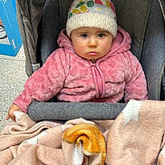 Adriana a rejoint le concours — aidez-le/la à gagner de superbes lots ! baby, baby_face, blanket, bundle, child, cozy, cute, expression, face, hat, indoor, infant, knit_hat, person, pink_jacket, seated, soft_texture, star_pattern, stroller, warm_clothing