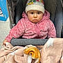 baby, child, stroller, blanket, hat, pink_jacket, face, expression, indoor, warm_clothing, cozy, knit_hat, person, seated, infant, baby_face, soft_texture, bundle, cute, star_pattern
