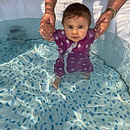 Adriana a rejoint le concours — aidez-le/la à gagner de superbes lots ! toddler, baby, child, swimsuit, water, pool, adult_hands, sunlight, reflection, outdoor, playing, summer, splash, holding_hands, purple_clothing, polka_dot, cute, face, feet, fun