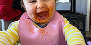 Adriana a rejoint le concours — aidez-le/la à gagner de superbes lots ! toddler, child, happy, smiling, messy_face, bib, yellow_striped_shirt, table, wooden_table, indoor, home, highchair, food_stains, reaching, face, person, cute, baby, clothing, portrait