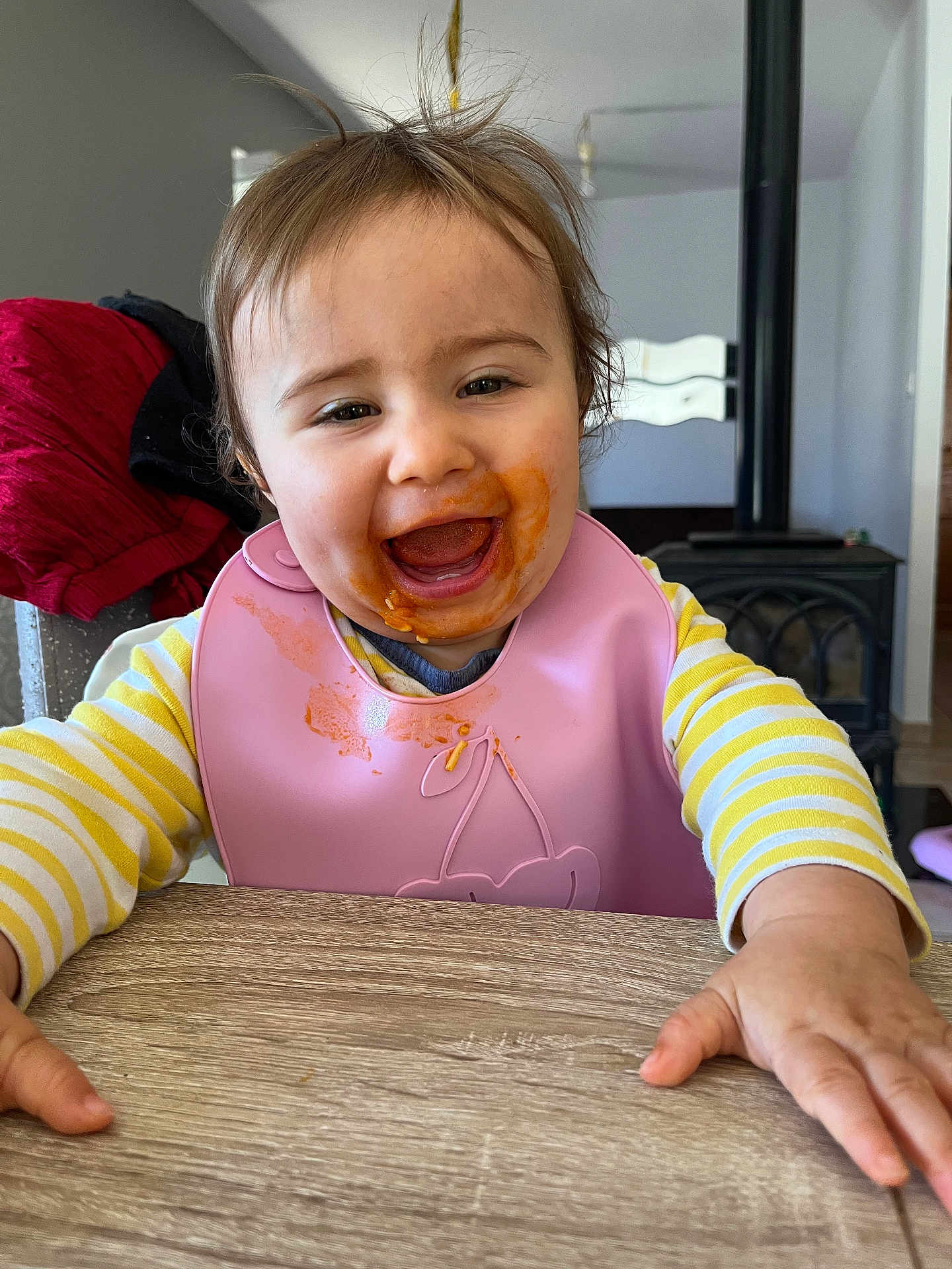 Adriana a rejoint le concours — aidez-le/la à gagner de superbes lots ! toddler, child, happy, smiling, messy_face, bib, yellow_striped_shirt, table, wooden_table, indoor, home, highchair, food_stains, reaching, face, person, cute, baby, clothing, portrait