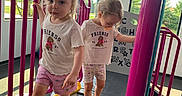 Lily joined the competition — help win amazing prizes! alphabet_board, blonde_hair, blue_poles, casual_clothing, children, climbing_structure, daylight, indoor_playground, pink_railings, play_equipment, playground, shorts, siblings, smiling, sneakers, standing, t_shirts, toddlers, walking, windows