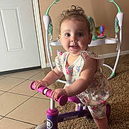 Ashly joined the competition — help win amazing prizes! baby, barefoot, big_eyes, candid, carpet, child, curly_hair, door, exersaucer, floral_dress, hands, indoors, playroom, portrait, ride_on_toy, smile, tile_floor, toddler, toy, tricycle