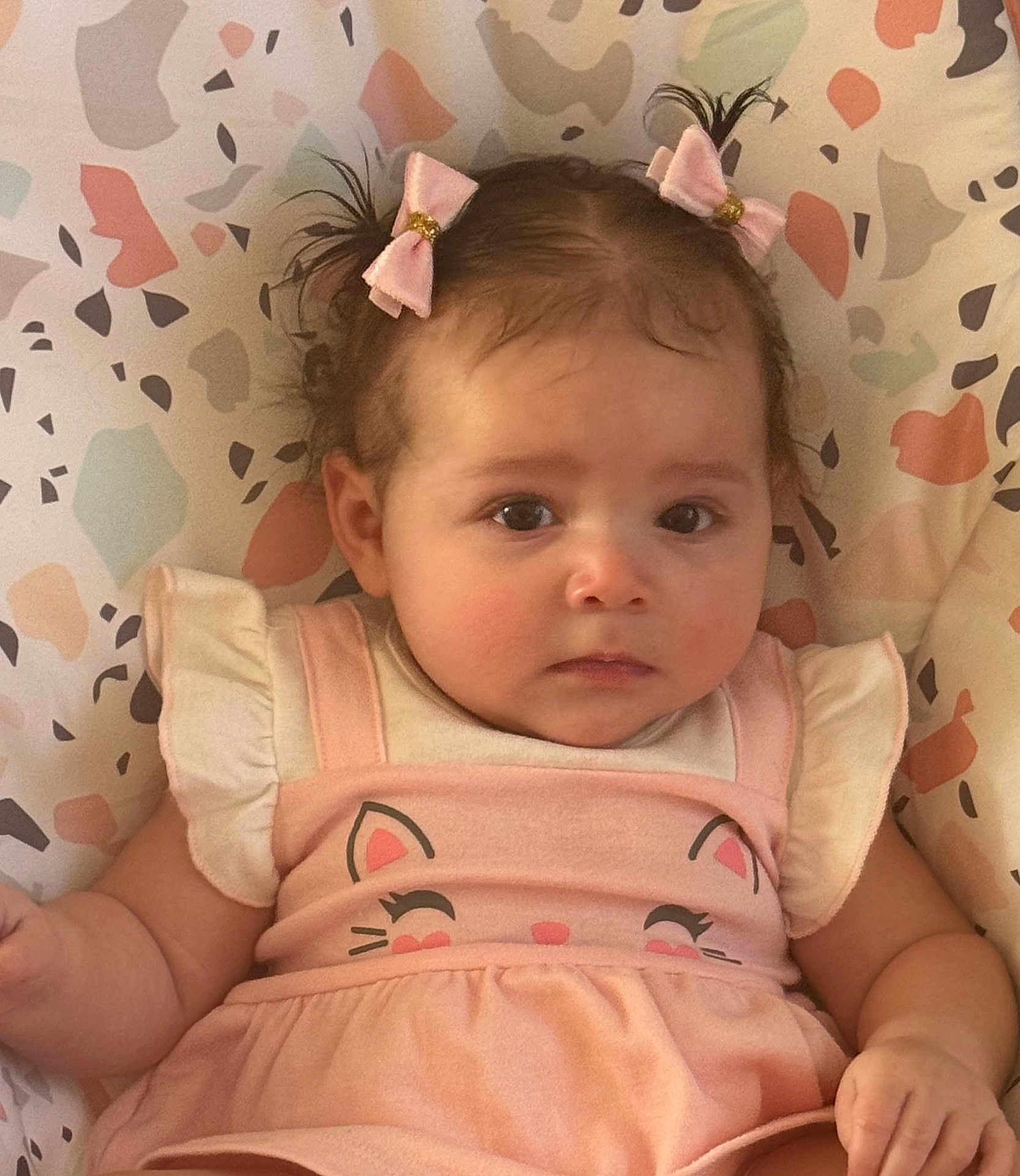 Ashly is registered to the contest to win money with this photo: baby, child, pink_bows, pink_dress, cat_design, infant, cute, portrait, face, hair, patterned_background, sitting, closeup, adorable, young_child, clothing, expression, indoor, skin, person