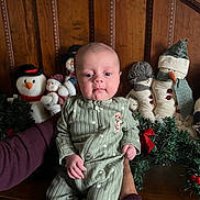 Lucas joined the competition — help win amazing prizes! baby, infant, child, green_onesie, gingerbread_patch, hands, snowman_dolls, holiday_decor, garland, wooden_background, festive, indoor, portrait, cute, calm, person, face, smile, christmas, seasonal