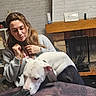 Athéna participe au concours pour gagner de l'argent avec cette photo : woman, dog, indoor, table, coffee, snack, box, fireplace, brick_wall, sweatshirt, curious, cup, wrapped_snack, sitting, home, shelf, casual, brown_hair, relaxed, interaction