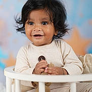 Akshiv is registered to the contest to win money with this photo: toddler, child, baby, smiling, black_hair, indoors, crib, toy, knitted_toy, pastel_background, happy, portrait, cute, sitting, infant, clothing, long_sleeves, soft_lighting, face, young_child