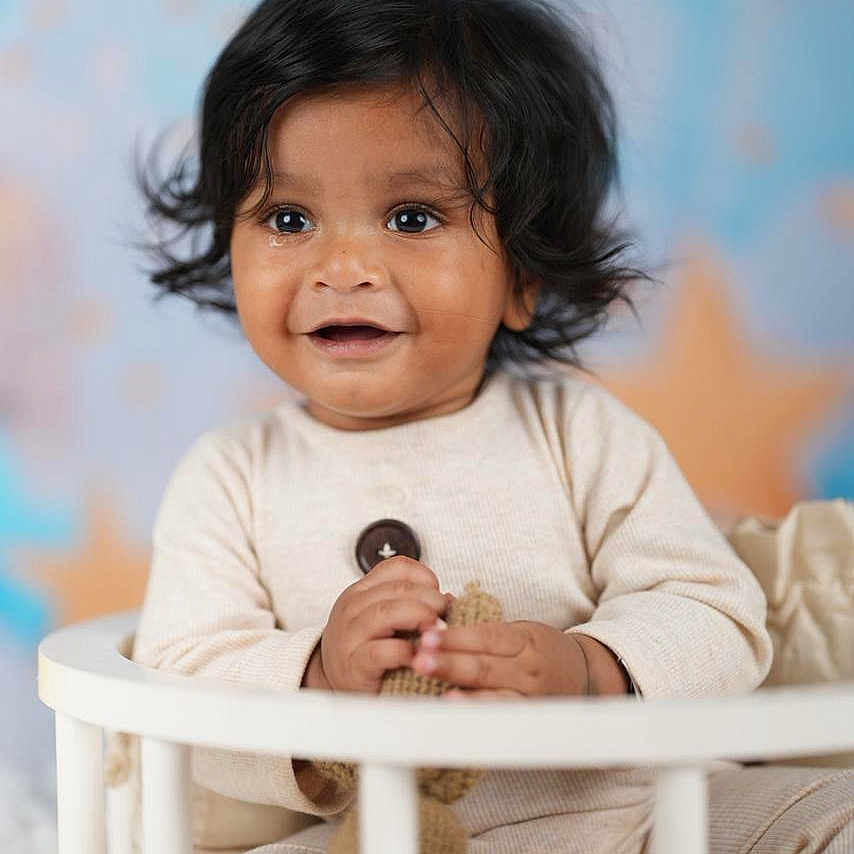 Akshiv is registered to the contest to win money with this photo: toddler, child, baby, smiling, black_hair, indoors, crib, toy, knitted_toy, pastel_background, happy, portrait, cute, sitting, infant, clothing, long_sleeves, soft_lighting, face, young_child