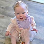 Aurora is registered to the contest to win money with this photo: baby, child, girl, pink_bow, lavender_bib, tutu, sitting, floor, indoor, cute, smiling, curious, hand, legs, toy, pastel_colors, soft_lighting, portrait, infant, happy