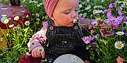 Aurora is registered to the contest to win money with this photo: baby, child, infant, milestone_sign, 10_months, headband, denim_overalls, flowers, garden, mushroom_statue, nature, outdoor, greenery, pink, cute, sitting, barefoot, plants, sunlight, portrait