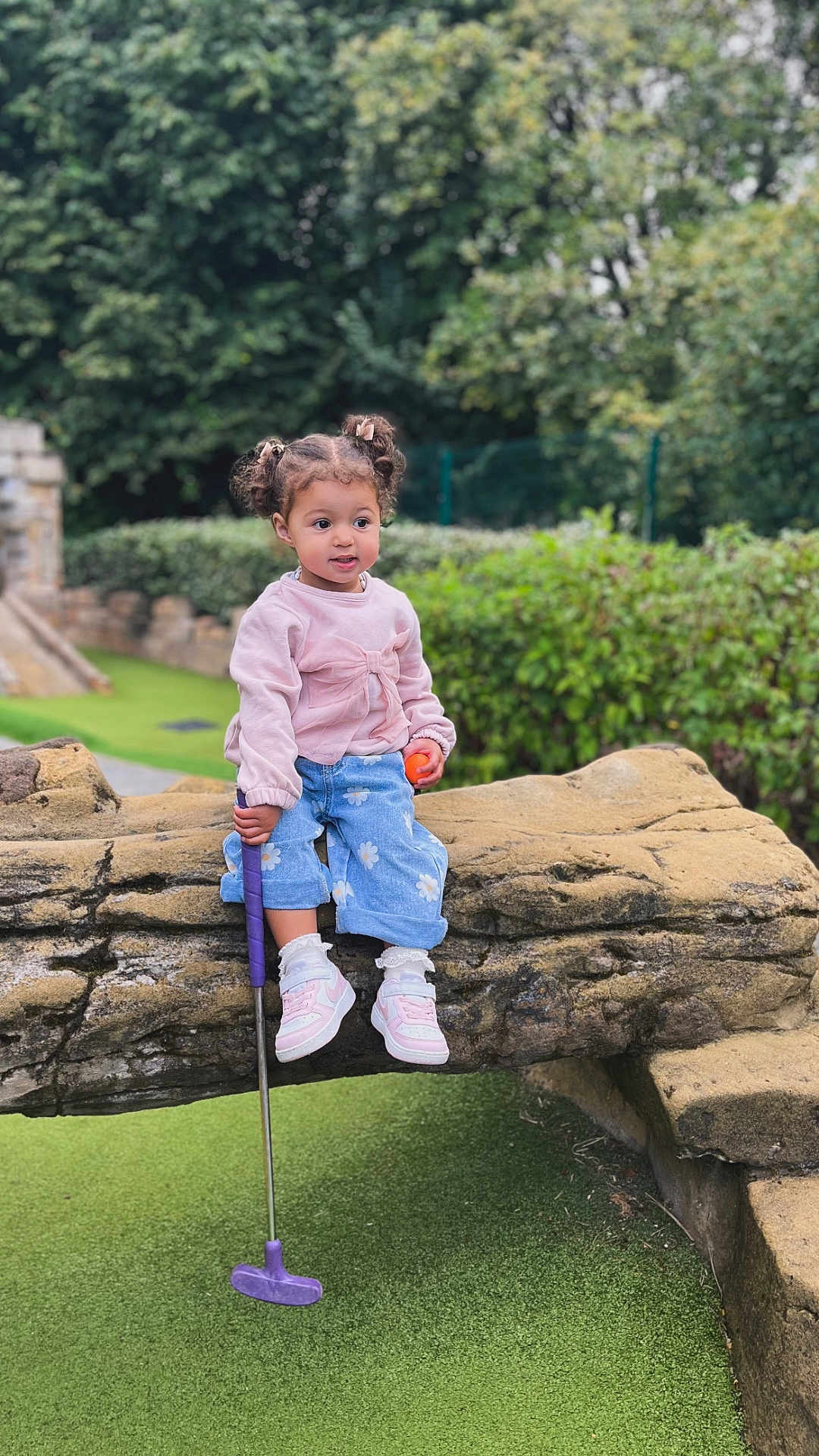 Aayla-Louise joined the competition — help win amazing prizes! toddler, child, girl, outdoor, mini_golf, putter, golf_ball, stone_bridge, greenery, casual_clothing, pink_sweater, blue_jeans, shoes, curly_hair, pigtails, playground, nature, recreation, young_child, park