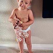 Sofia is registered to the contest to win money with this photo: toddler, child, baby, diaper, barefoot, plush_toy, giraffe_toy, carpet, standing, smiling, cute, indoor, wall, texture, light, person, young_child, innocent, happy, playful