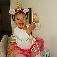 Beatrice participe au concours pour gagner de l'argent avec cette photo : child, toddler, smile, unicorn_headband, wand, tutu, sitting, indoor, happy, curly_hair, white_top, pink_tights, chair, playful, toy, portrait, accessory, room, baby_wipes, laughing
