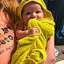 Amyra joined the competition — help win amazing prizes! baby, child, towel, yellow, hooded_towel, red_bow, person, holding, indoor, curious_eyes, peach_shirt, text_on_shirt, arm, face, cute, soft_texture, bath_time, close_up, infant, smiling