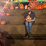 man, baby, pumpkins, jack_o_lanterns, bleachers, sign, night, lighting, orange_clothing, fall, festival, smile, casual_clothing, beard, hat, celebration, outdoor, wood, event, people