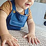 toddler, child, baby, face, hands, overalls, brown_shirt, indoor, home, plant, decor, textured_surface, smile, curious, portrait, young_child, crawling, cute, light, closeup