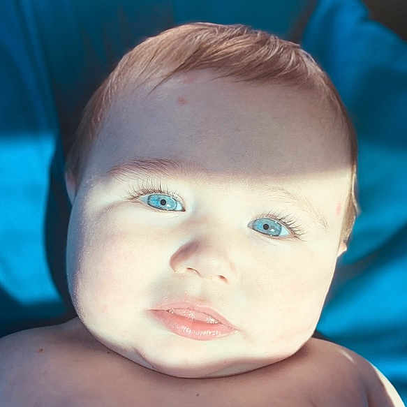 Zaylen joined the competition — help win amazing prizes! baby, blue_eyes, close_up, face, child, infant, light_shadow, portrait, skin, hair, expression, looking_at_camera, natural_light, background, blue_background, cute, young_child, head, indoors, soft_light