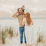 family, beach, baby, man, woman, sand, grass, ocean, sky, clouds, barefoot, casual_clothing, happy, playful, outdoor, portrait, smile, child, headband, nature