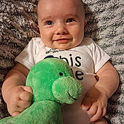 Elvis joined the competition — help win amazing prizes! baby, blanket, child, comfort, cozy, cute, face, green_toy, hands, happy, indoors, infant, lying_down, plush_toy, portrait, smile, soft_texture, toddler, white_onesie, young_child
