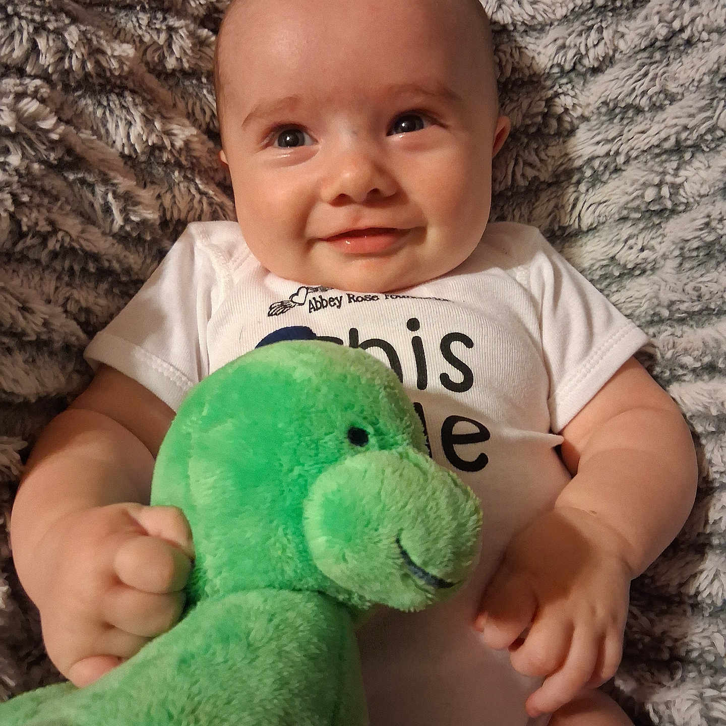 Elvis joined the competition — help win amazing prizes! baby, blanket, child, comfort, cozy, cute, face, green_toy, hands, happy, indoors, infant, lying_down, plush_toy, portrait, smile, soft_texture, toddler, white_onesie, young_child