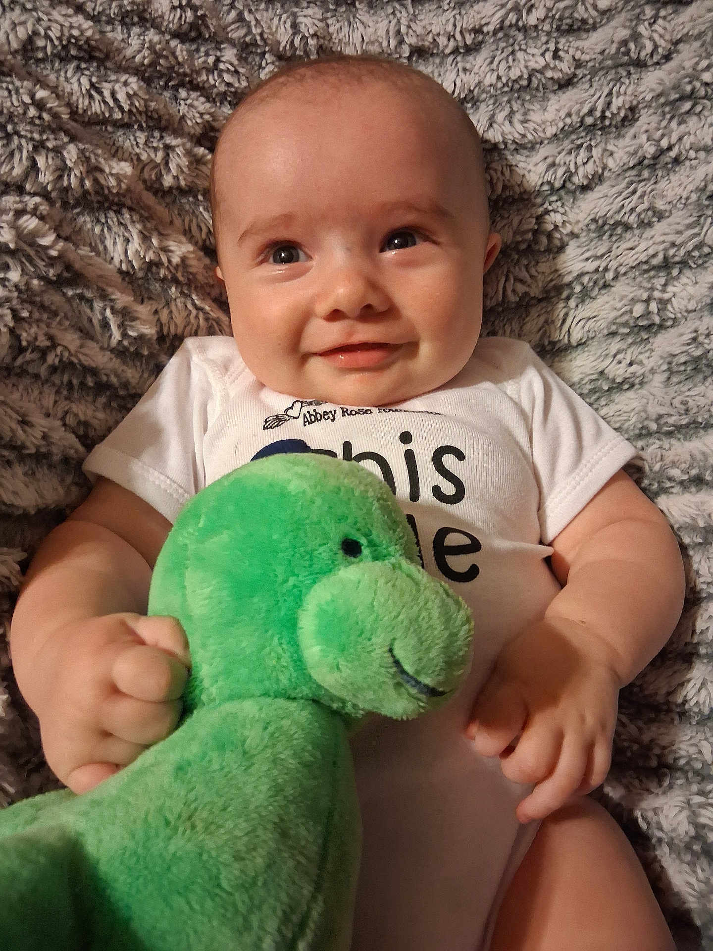 Elvis joined the competition — help win amazing prizes! baby, blanket, child, comfort, cozy, cute, face, green_toy, hands, happy, indoors, infant, lying_down, plush_toy, portrait, smile, soft_texture, toddler, white_onesie, young_child