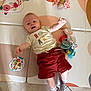 baby, child, play_mat, toy, stuffed_animal, indoor, smiling, shorts, socks, clothing, floor, happy, infant, colorful, arm_raised, lying_down, head, face, person, cute